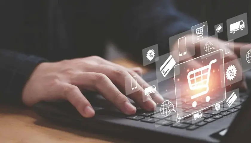 Dłoń na klawiaturze laptopa, nad nią ikony symbolizujące zakupy online: koszyk, karty płatnicze, dostawa. Sukces każdego ecommerce retailer.