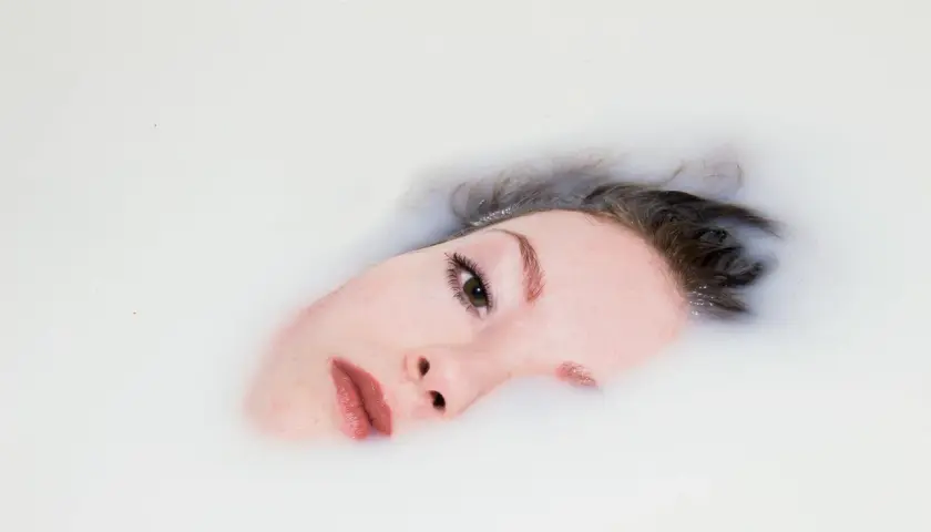 Rostro de mujer sumergido en leche, parte de un ritual de doble limpieza para una piel radiante.