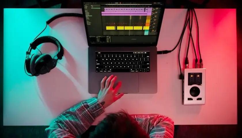 Person am Schreibtisch mit Kopfhörern, Laptop und Audio-Interface. Musikproduktion in 24 bit 48 khz.