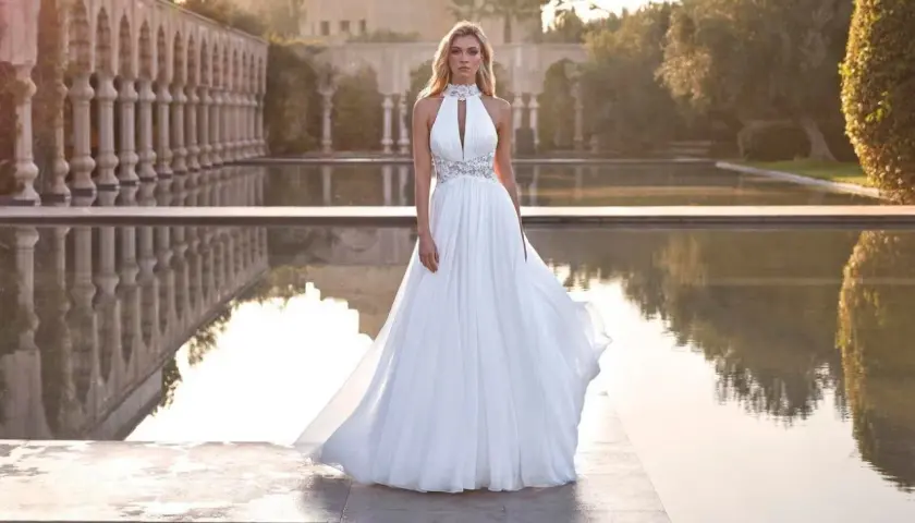 Piękna panna młoda w zwiewnej sukni czeka na swojego wybranka. Romantyczny ślub w plenerze, z wodą i architekturą w tle.