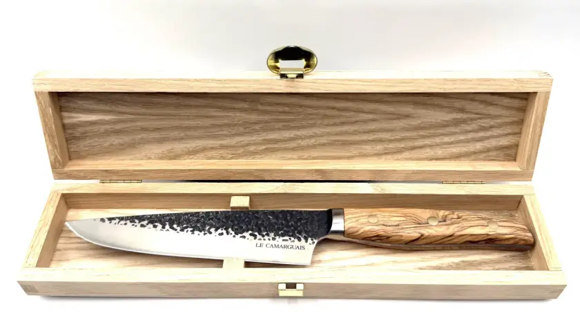 Un magnifique couteau au barbecue, avec une lame martelée et un manche en bois d'olivier, repose dans son coffret en bois.