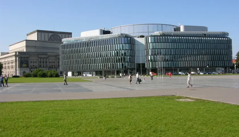Plac Piłsudskiego w Warszawie. Nowoczesny budynek z przeszkloną fasadą obok klasycystycznego gmachu.