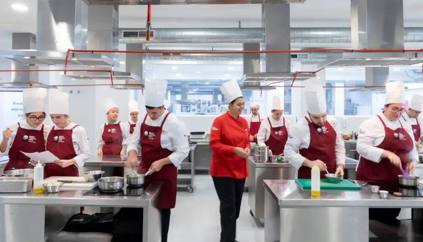 Estudiantes en un centro culinario mediterráneo, con toques rojos y blancos, aprendiendo a cocinar.