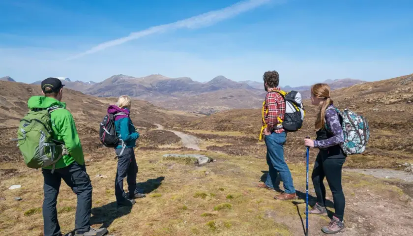 Four hikers enjoy a scenic view on Scotland hiking trips, with mountains stretching into the distance under a clear blue sky.