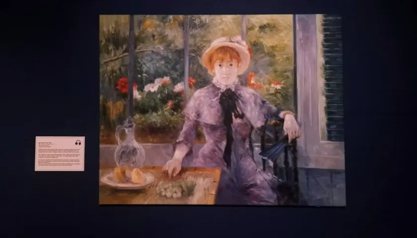 Auguste Renoir dzieła: portret młodej kobiety w kapeluszu, siedzącej przy stole z owocami i dzbankiem, w otoczeniu kwitnącego ogrodu.