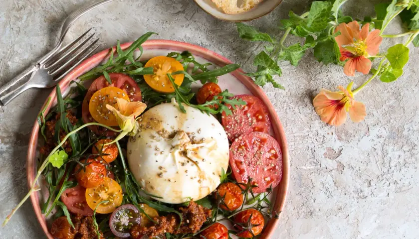 Ein bunter Tomaten Burrata Salat mit Rucola und essbaren Blüten.