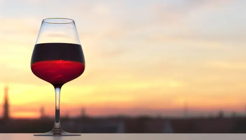 Verre de vin rouge bordeaux, parfait pour apprécier sa température idéale au coucher du soleil.