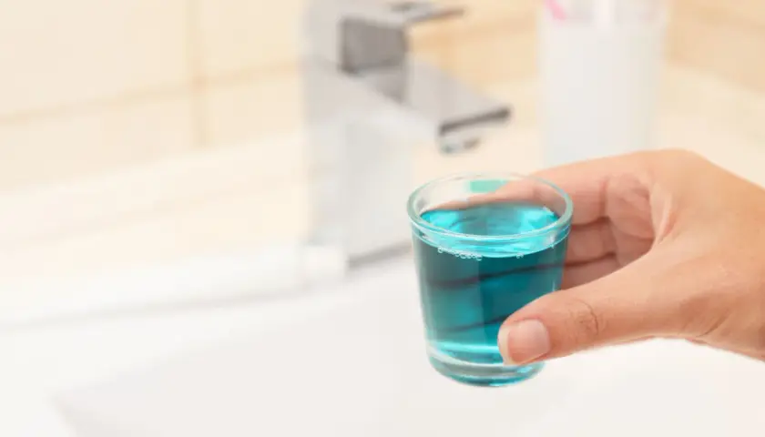Mano tiene bicchierino con collutorio azzurro, ideale per l'igiene orale in gravidanza.