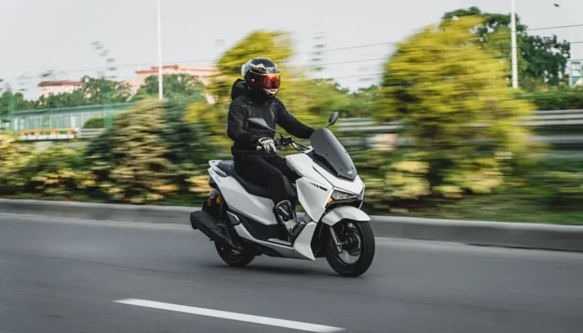 Hombre con casco y chaqueta negra conduce una moto 125 blanca por la autopista, demostrando que una moto 125 puede ir por autopista.