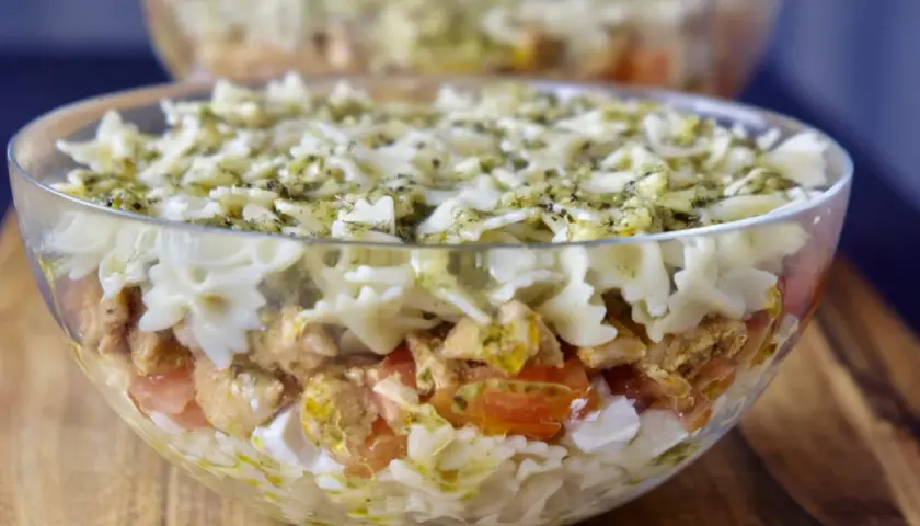 Pyszna, warstwowa sałatka z kurczakiem i makaronem farfalle, polana sosem pesto. Idealna na najlepsza sałatka z kurczakiem na imprezę!