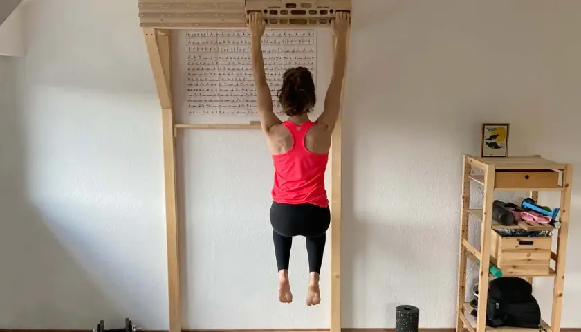 Frau hängt an einem Hangboard für intensives **Hangboard Training**. Trainingsplan hängt an der Wand.