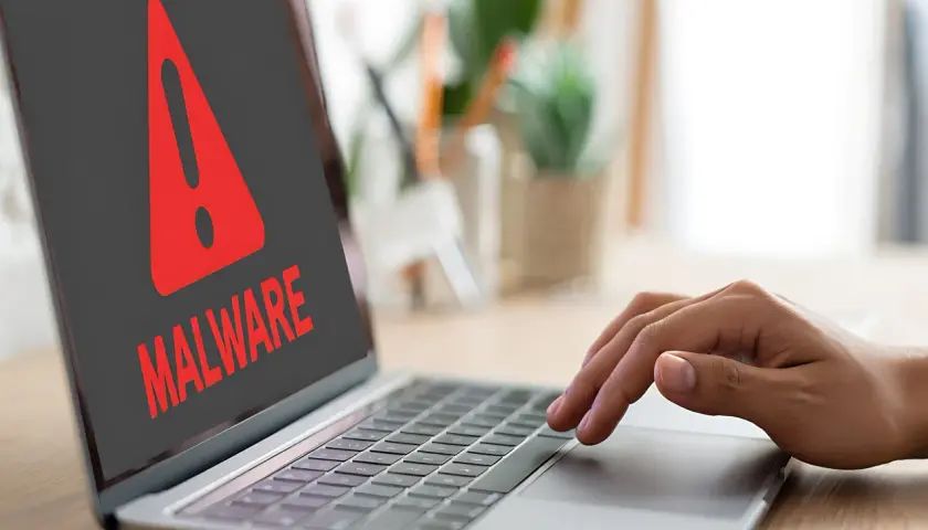 Ostrzeżenie na ekranie laptopa: "MALWARE". Dłoń użytkownika zbliża się do klawiatury, być może próbując dowiedzieć się, spyware co to jest i jak się przed nim chronić.