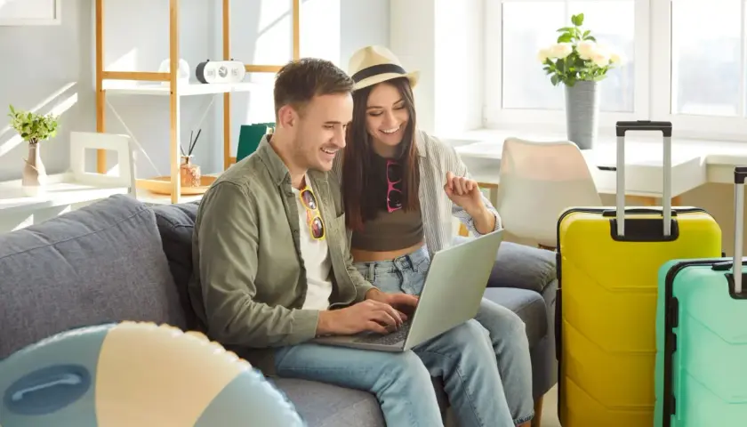 Para, planując kiedy majówka, przegląda oferty wakacyjne na laptopie. Obok walizki czekają na podróż.