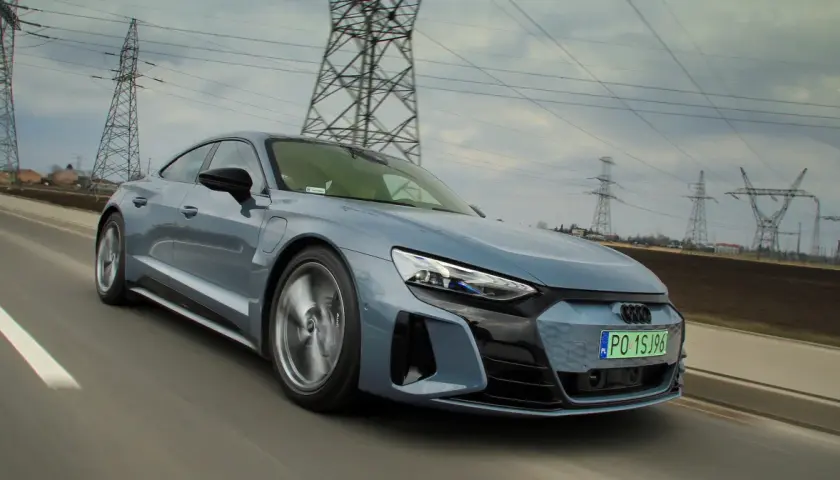 Szary Audi e-tron GT pędzi po drodze, otoczony liniami energetycznymi i słupami wysokiego napięcia.