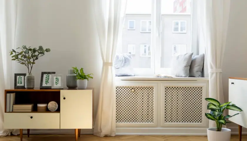 Elegancka osłona kaloryfera pod oknem, z ażurowym wzorem, stanowi stylowe rozwiązanie, jak zasłonić kaloryfer pod oknem, dodając wnętrzu uroku.
