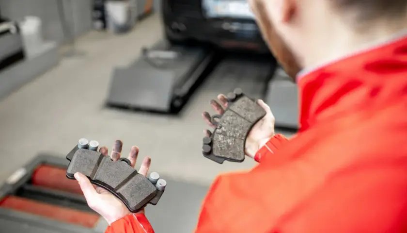 Mechanik pokazuje zużyte klocki hamulcowe, które mogą powodować syczenie przy wciskaniu hamulca.