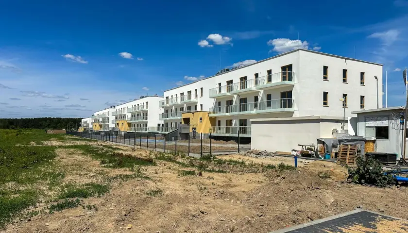Nowe osiedle z białymi budynkami i balkonami, otoczone zielenią i placem budowy. To przyszłe eco berensona.