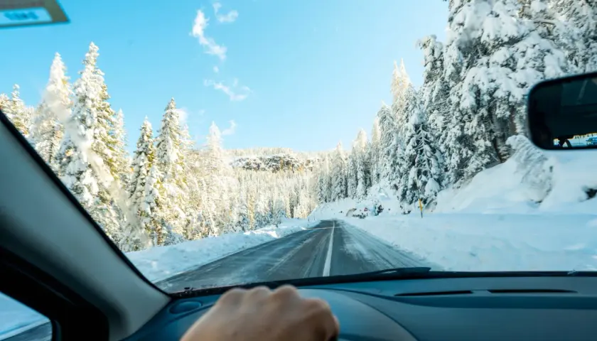 Conduciendo por una carretera nevada, rodeada de árboles cubiertos de blanco. Consejos para como conducir con nieve.