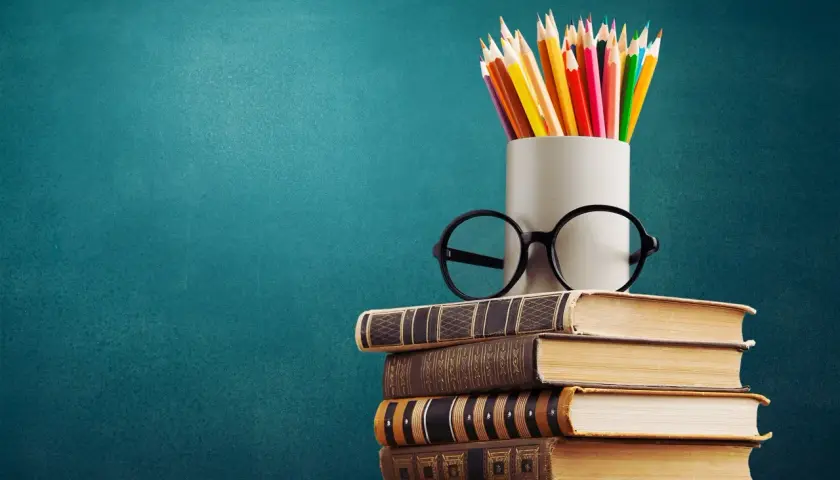 Stos książek, okulary i kredki na tle tablicy. To symbol wiedzy, która otwiera drzwi do kariery, nawet jeśli to co to znaczy wykształcenie średnie branżowe.