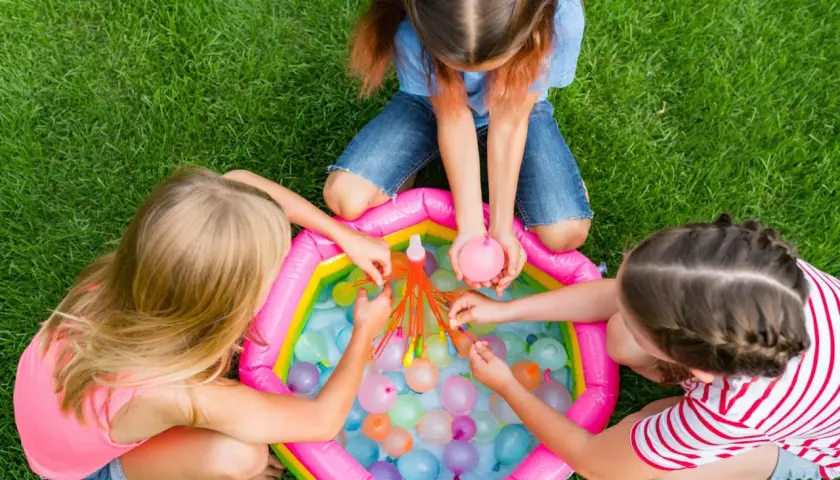 Bambine giocano con palloncini d'acqua in una piscina gonfiabile, perfetti giochi per feste di compleanno 7-8 anni.