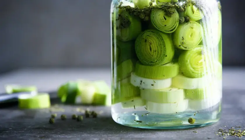 Ein Glas mit geschnittenem Lauch, bereit zum lauch fermentieren. Grüne Pfefferkörner und Kräuter sind ebenfalls zu sehen.