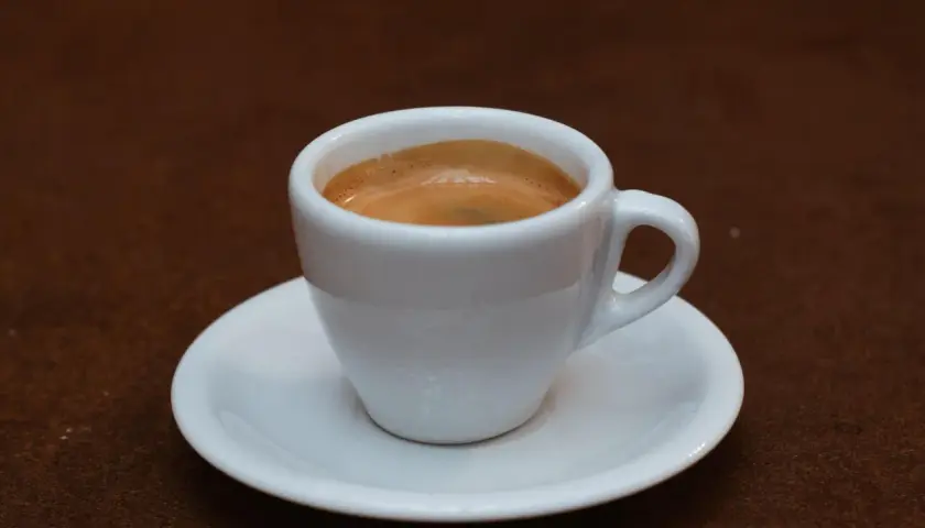 Ein weißer Becher mit cremigem, doppeltem Espresso steht auf einer Untertasse.