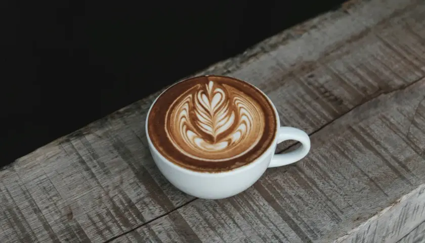 Eine Tasse Cappuccino mit Latte Art auf einem Holztisch. Die Menge des Kaffees ist perfekt für einen Genussmoment.