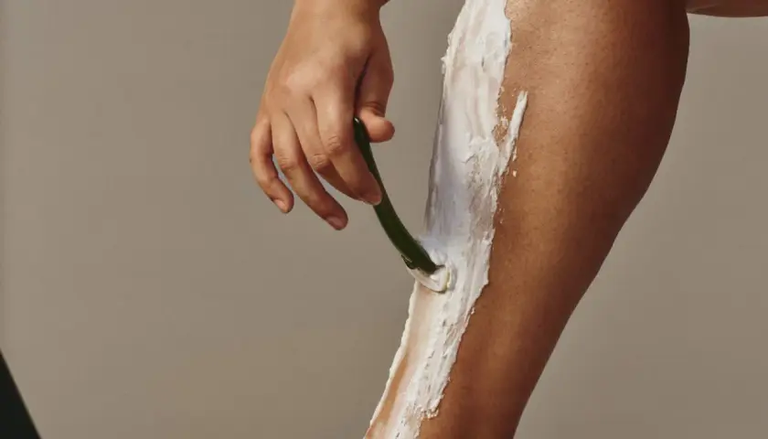 En hand rakar ett ben täckt av raklödder, för att undvika strawberry legs.