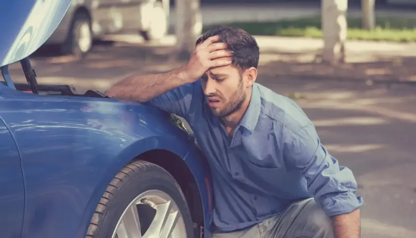 Hombre frustrado con el capó abierto de su coche azul. A veces, merece la pena arreglar un coche de 20 años.