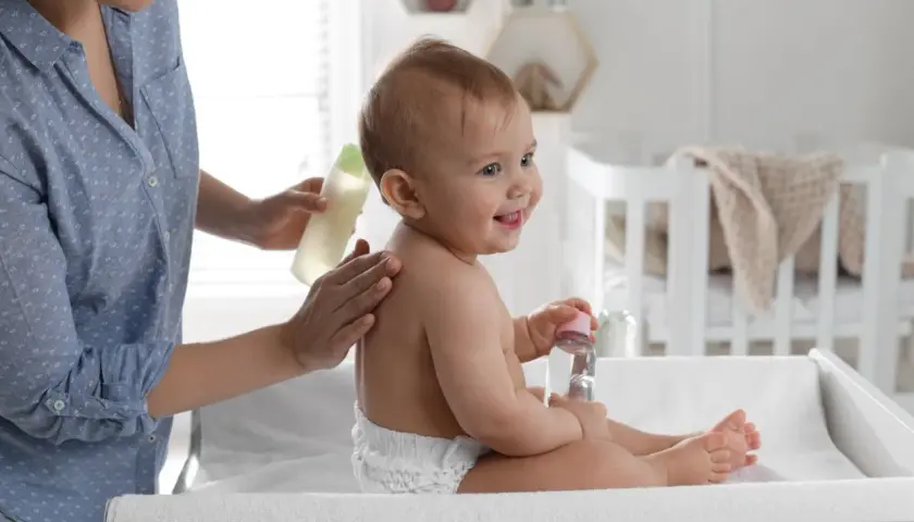 Mama delikatnie wmasowuje w plecy dziecka olejek migdałowy do kąpieli. Uśmiechnięty maluch trzyma buteleczkę z płynem.