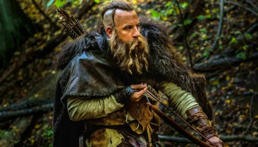 En skäggig krigare med pilbåge i en skog, redo för strid som den sista häxjägaren.