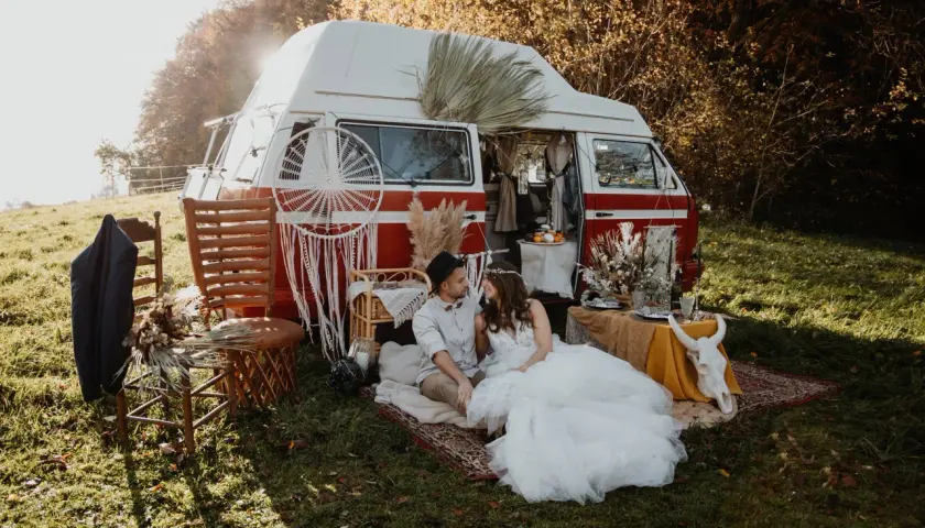 Un couple en tenue de mariage profite d'un mariage pique-nique champêtre près d'un van aménagé, décoré de style bohème.
