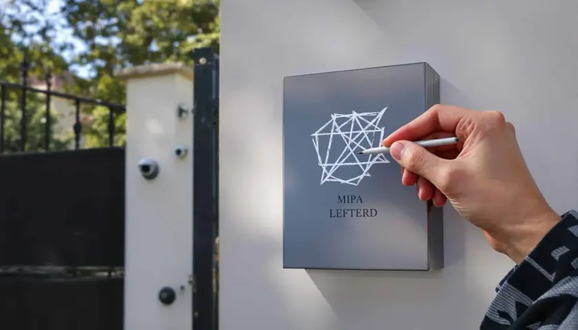 Main MIPA LEFTERD, une main trace un motif géométrique sur une plaque. Une caméra de surveillance est visible au-dessus, comme un marquage cambriolage discret.