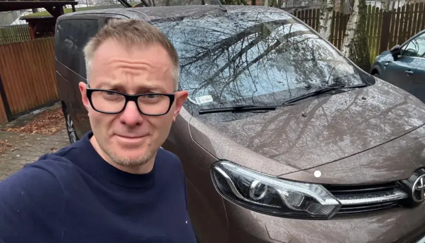 Mężczyzna w okularach przed brązowym vanem, gotowy do podpisania umowy komisu.