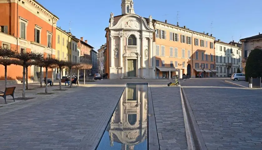 Piazza con chiesa barocca e specchio d'acqua, ideale per scoprire cosa vedere a Reggio Emilia in un giorno.