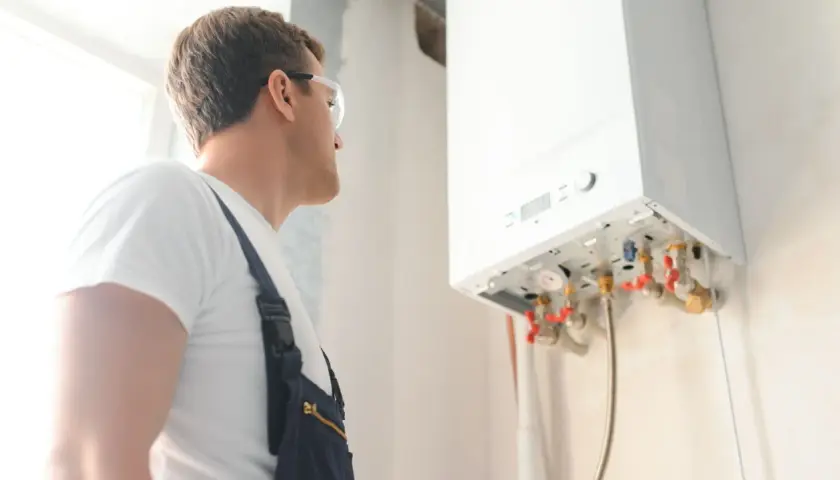 Technik w okularach ochronnych sprawdza instalację gazową. Wykonuje odpowietrzanie pieca gazowego, dbając o jego prawidłowe działanie.