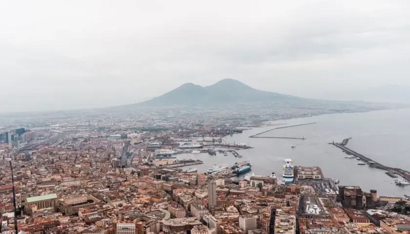 Panoramic view of Napoli, Naples, with Mount Vesuvius looming in the distance over the bustling port and city.