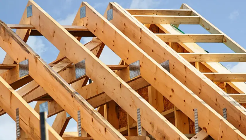 Structure en bois d'une charpente simple, avec des poutres assemblées par des équerres métalliques sous un ciel bleu.