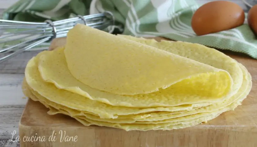 Una pila di crepes dorate su un tagliere di legno, pronte per essere farcite. La ricetta crepes perfetta per ogni occasione.