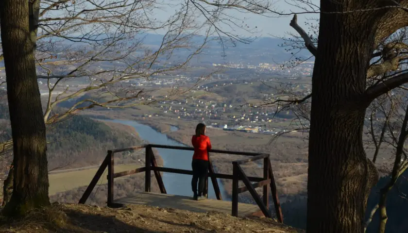 Widok z białowodzkiej góry na dolinę z rzeką i miasteczkiem. Kobieta w czerwonej bluzie podziwia panoramę.