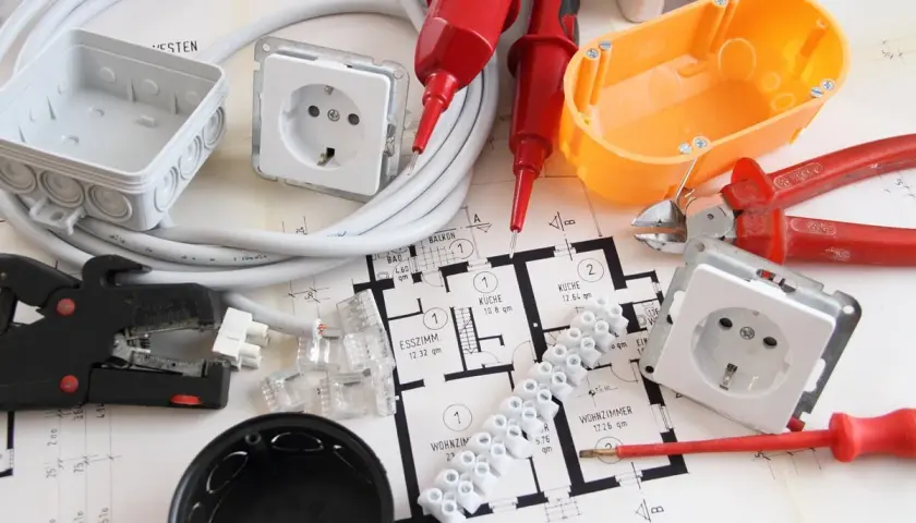 Narzędzia i materiały do wymiany instalacji elektrycznej bez kucia: przewody, puszki, gniazdka, złączki, kombinerki, ściągacz izolacji, śrubokręt i schemat instalacji.