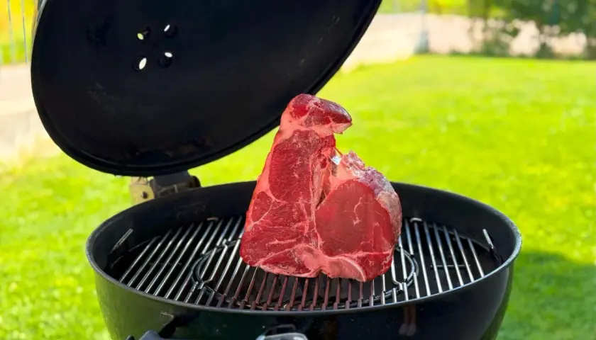 Una succulenta bistecca alla fiorentina cruda riposa sulla griglia di un barbecue, pronta per essere cucinata all'aperto.