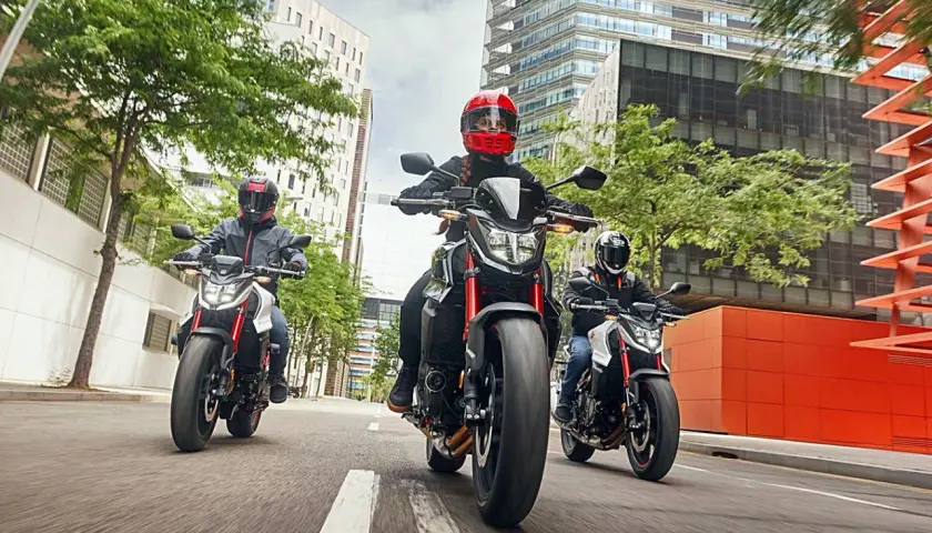 Tres motociclistas con cascos circulan en fila por una calle urbana. Una motocicleta puede circular por el arcén, ofreciendo agilidad entre el tráfico.