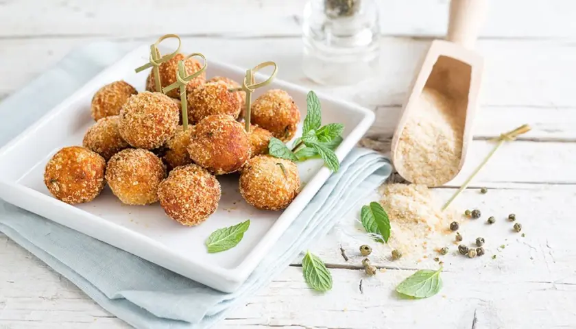 Deliziose polpette tonno e ricotta, dorate e croccanti, servite su un piatto bianco con menta fresca.