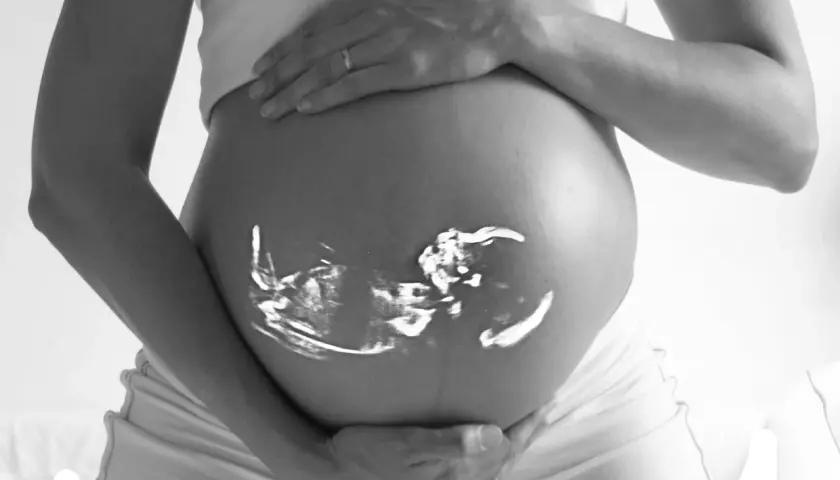 Gravid vecka 6 ultraljud projicerat på en gravid mage. En hand vilar på magen, en ring syns på fingret.