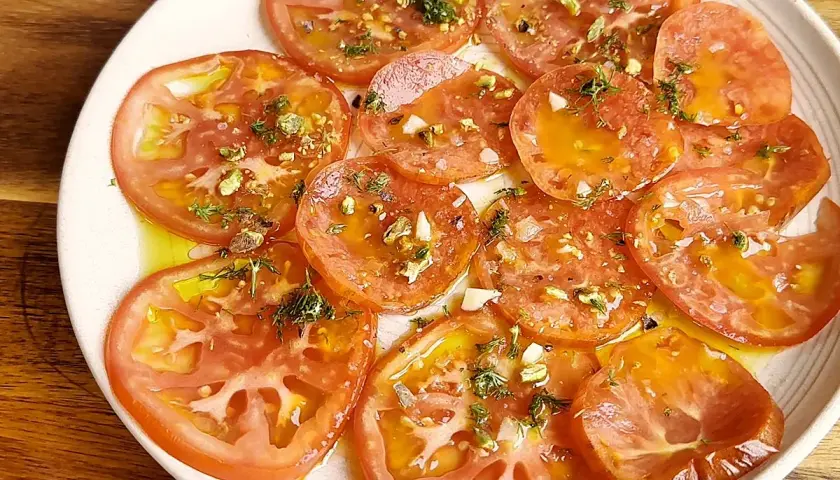 Carpaccio de tomate fresco con aceite de oliva, ajo picado y hierbas aromáticas. Un plato ligero y lleno de sabor.