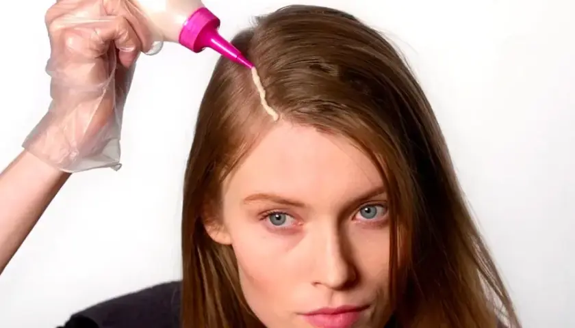 Mujer se aplica tinte en el cabello. Considera los tintes con amoniaco: ventajas y desventajas antes de usarlos.
