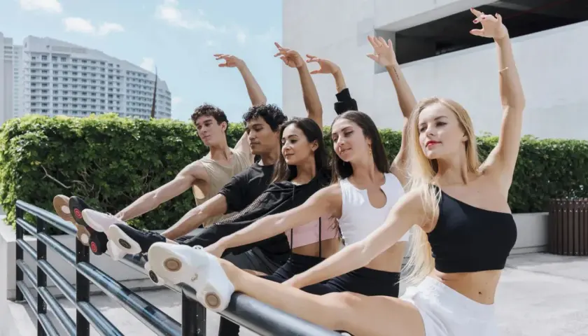 Giovani ballerini in una lezione di danza all'aperto, con un edificio moderno e vegetazione sullo sfondo.