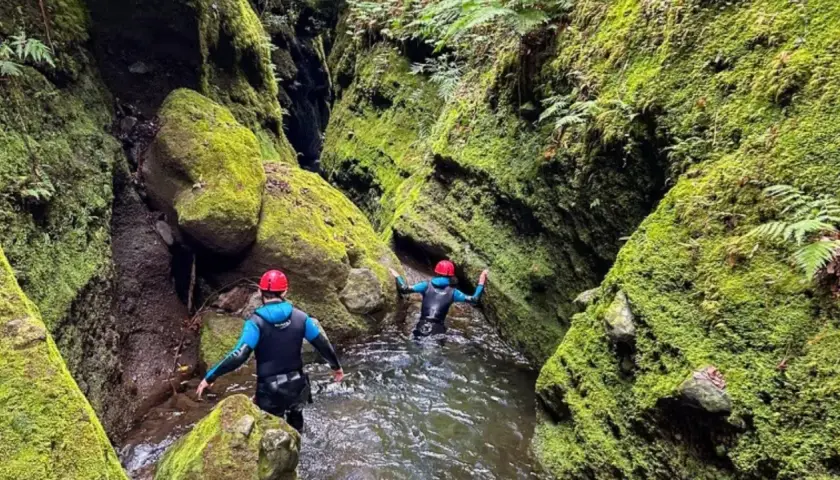 Dwie osoby w kombinezonach i kaskach przemierzają wąski, porośnięty mchem kanion. To właśnie jest canyoning!
