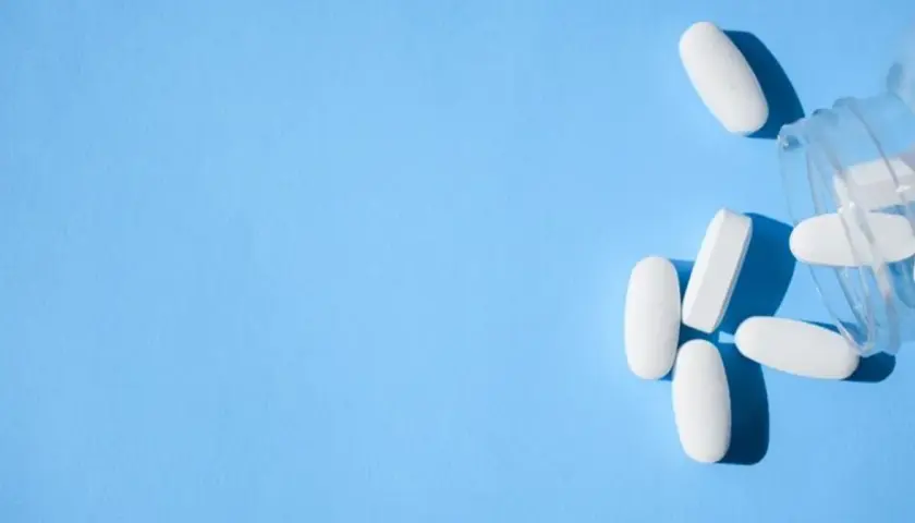 Białe tabletki, w tym oxycodone, wysypują się z przezroczystego pojemnika na niebieskim tle.